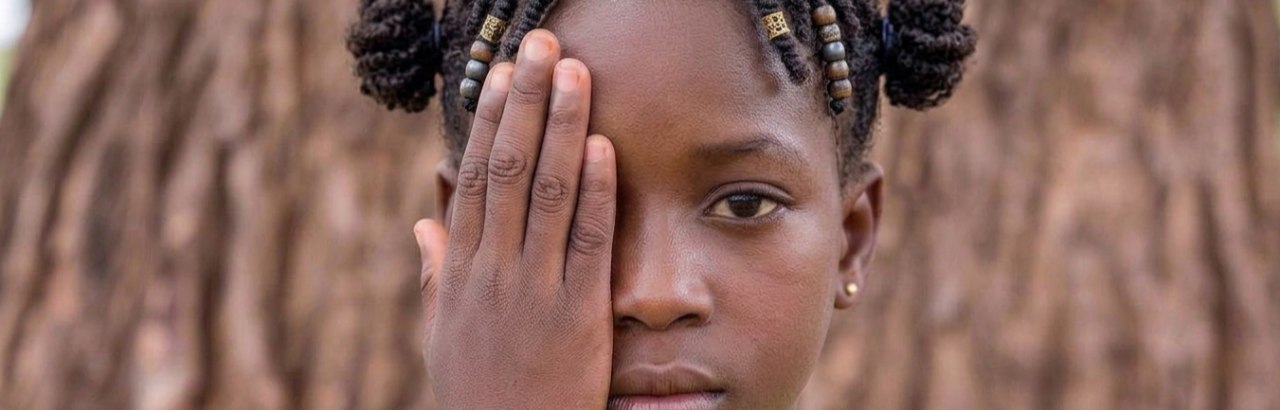 A young girl covers one eye with her hand during a vision screening, looking calmly at the camera.
